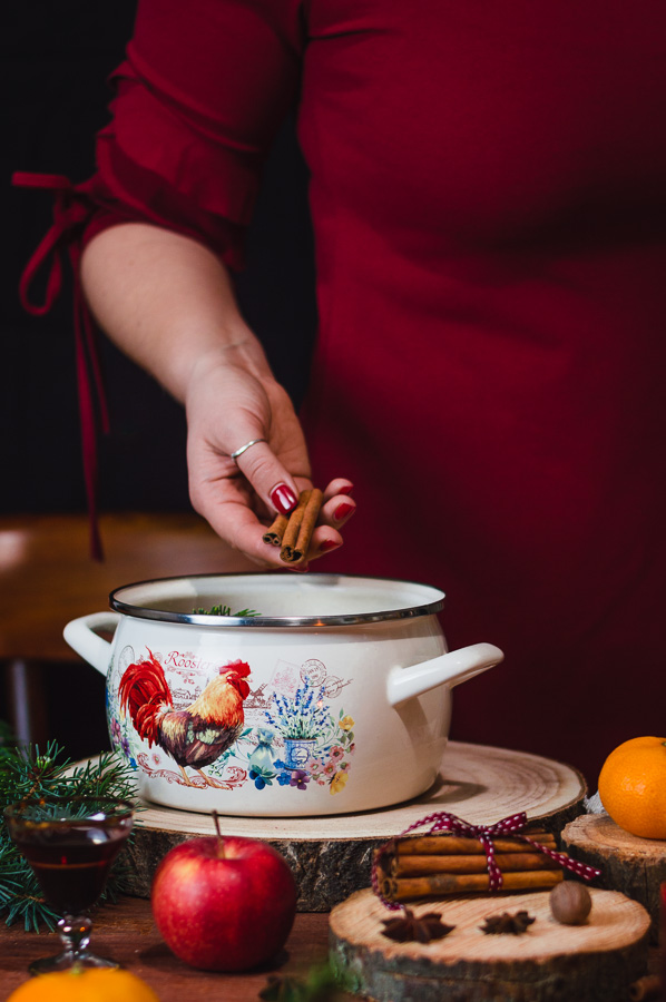 A woman throwing in cinnamon stick for making Christmas stovetop simmering pot