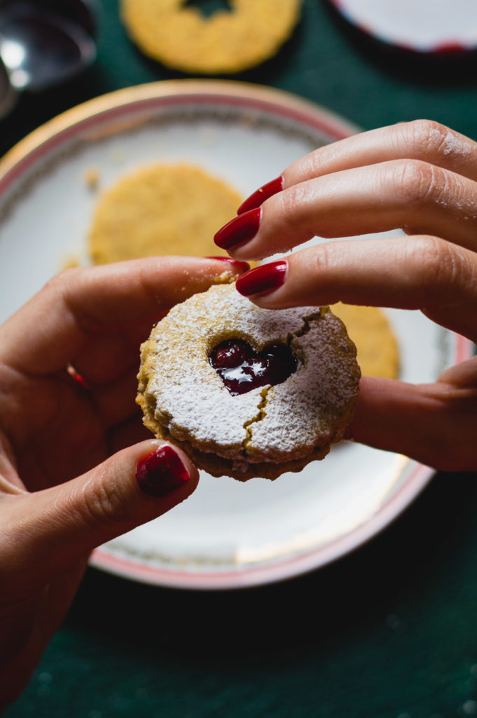 A woman holding a cracked Linzer cookie in her hands