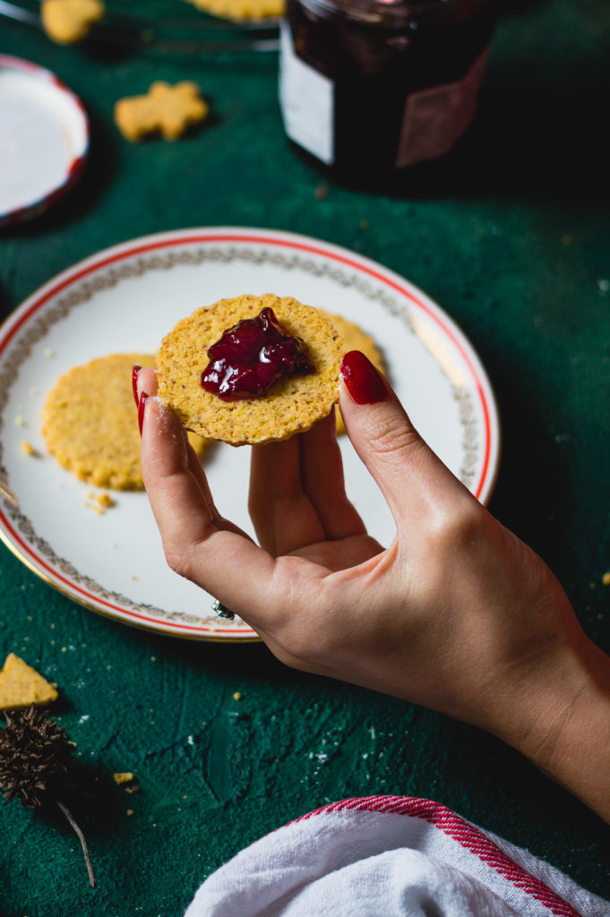 Woman holding half of a Linzer cookie in one hand with jam on it