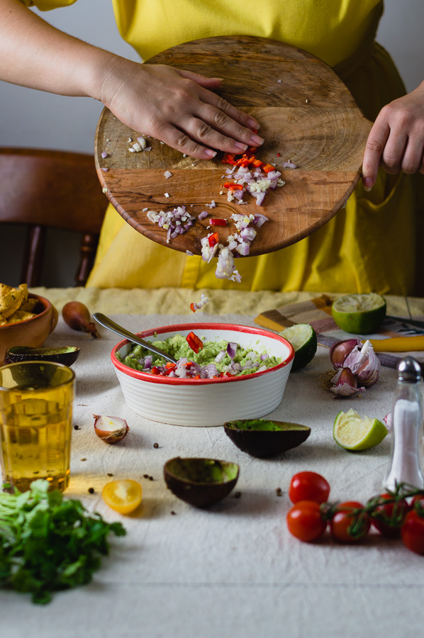 A woman adding onions, garlic and chili peppers in a bowl for making guacamole