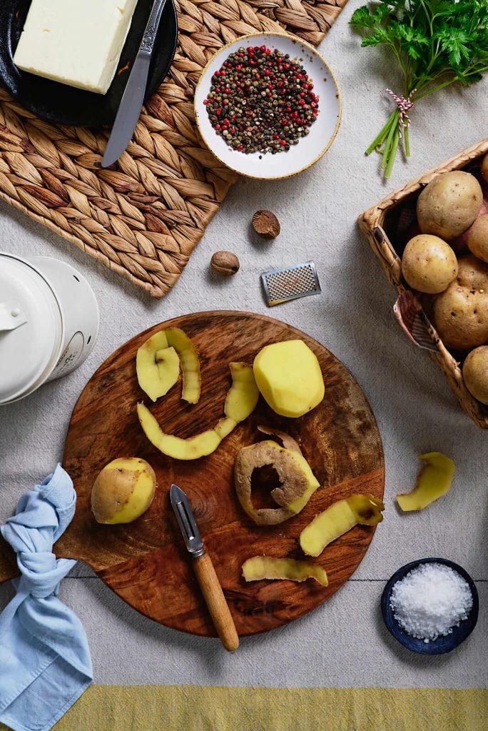 peeled potatoes on cutting board with ingredients for making mashed potatoes recipe