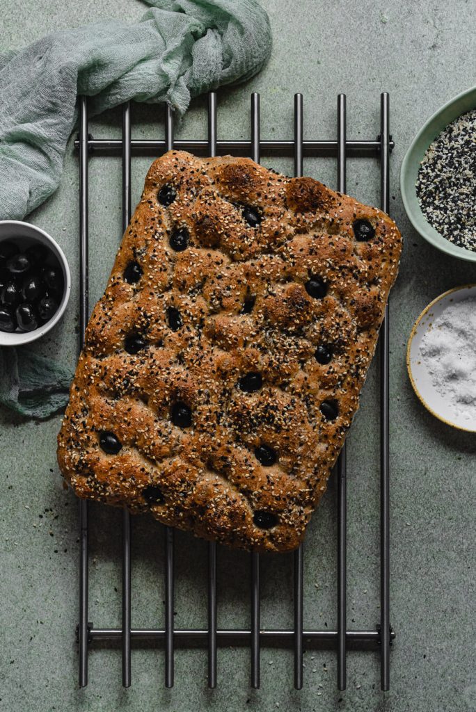 fresh out of the oven no knead whole wheat focaccia with black olives and seeds on a cooling rack