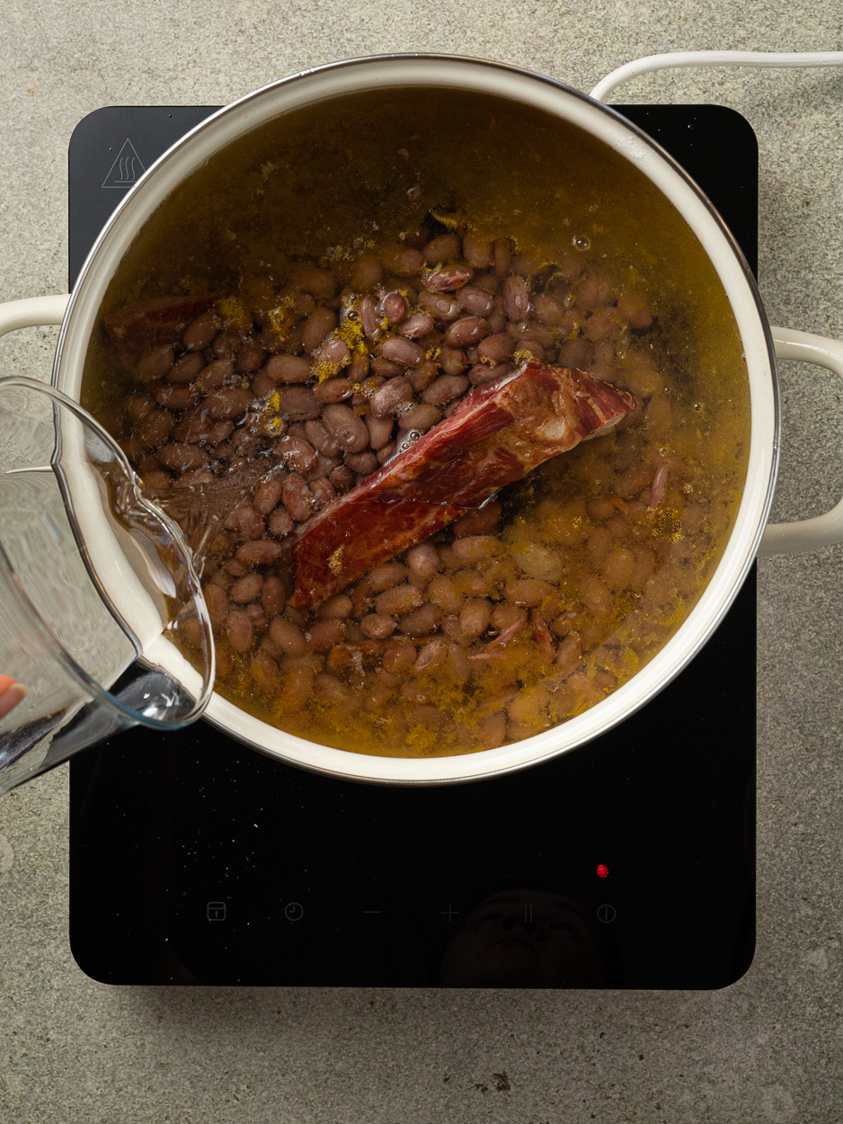 adding water to the pot with meat and beans