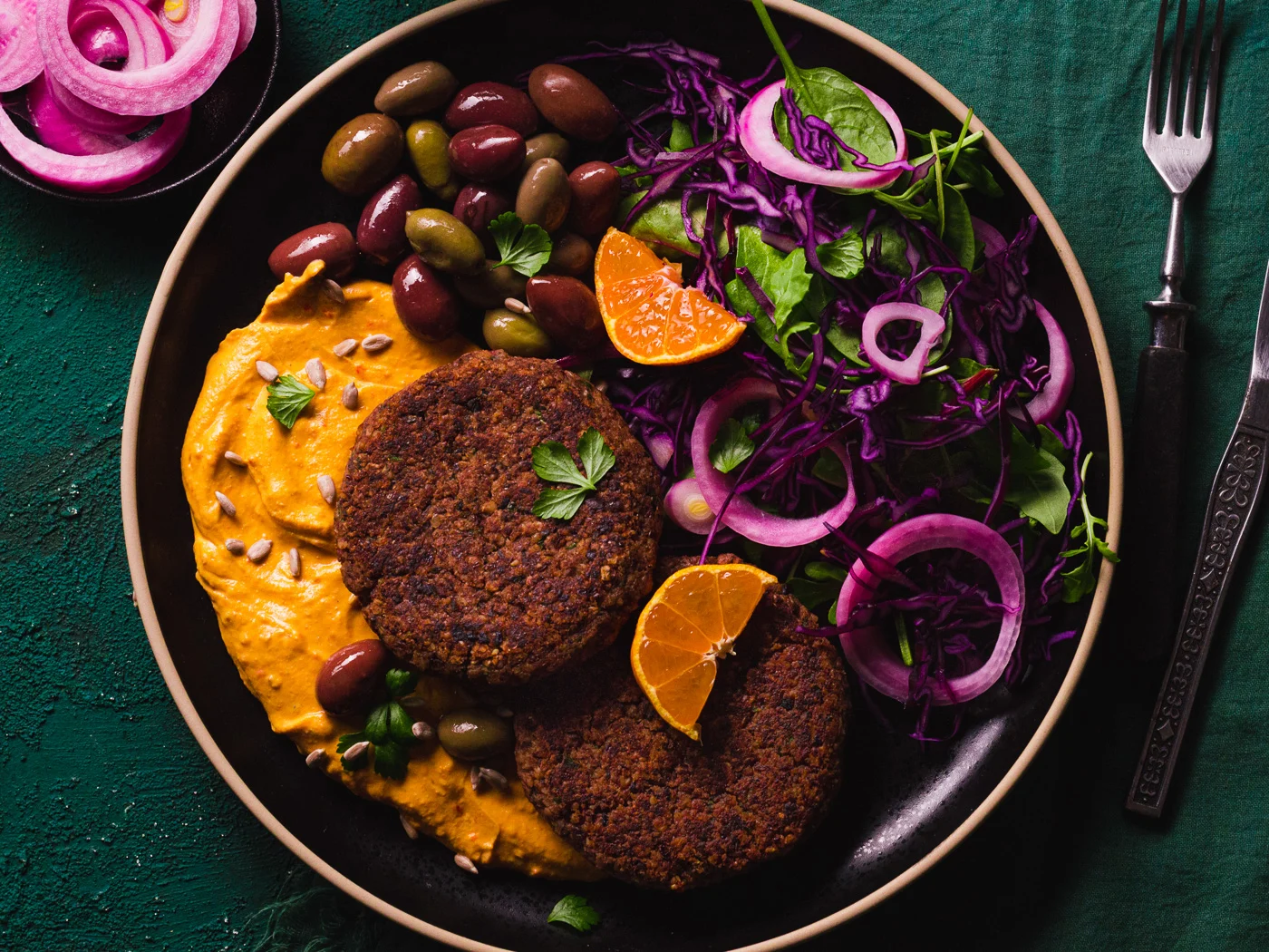 vegan mushroom and red bean patties served with some hummus, olives, pickled onion and salad.