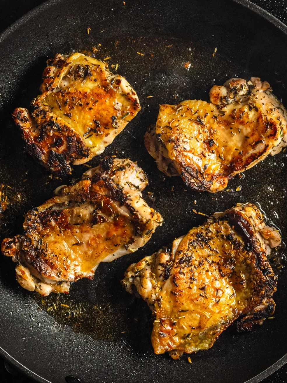 chicken thighs cooking in a pan until crispy and golden