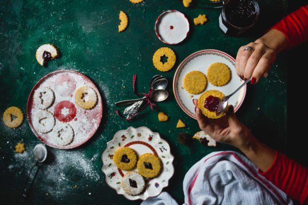 Young woman in red shirt putting jam on Christmas Linzer cookies